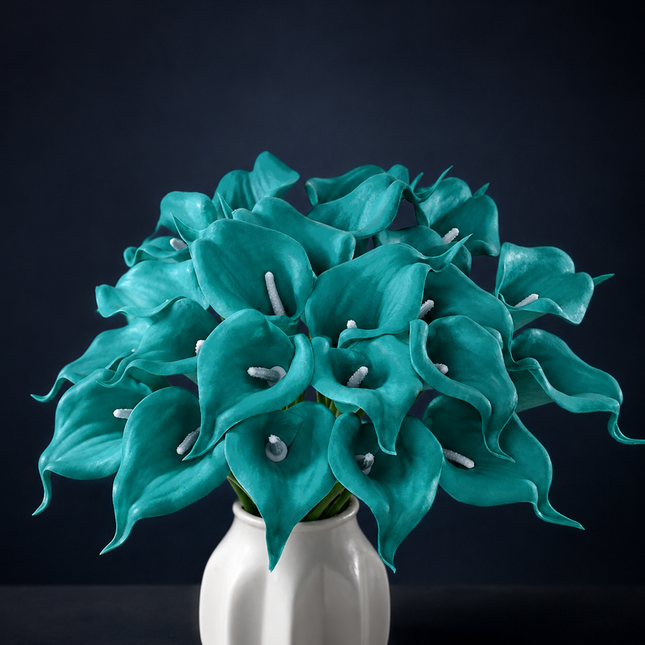 A vibrant teal calla lily bouquet in a glossy white ceramic vase, set against a dark navy blue background.